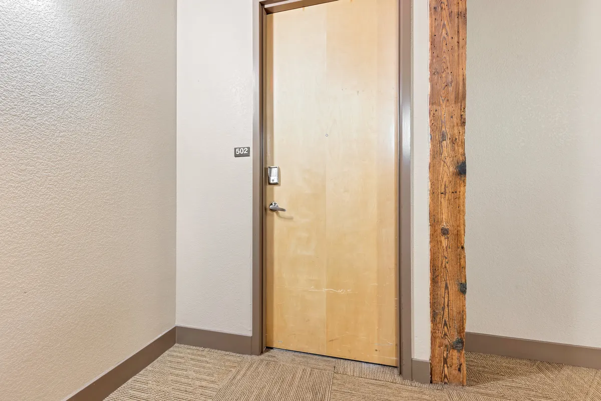 This image features the wooden front door with the apartment number '502' and a sturdy wooden beam, providing a clear visual of the threshold between the private home and the vibrant city outside. The scene captures the feeling of entering or leaving the apartment, making it highly relevant to the narrative of exploring the neighborhood.