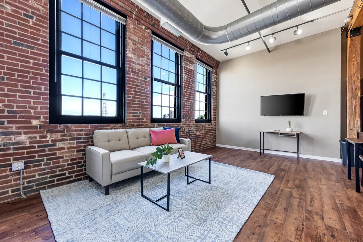 A cozy yet contemporary lounge setup is displayed, with a plush sofa, a coffee table, and floor-to-ceiling windows. The scene is ideal for intimate gatherings or quiet evenings, and the abundance of natural light showcases the architectural details.