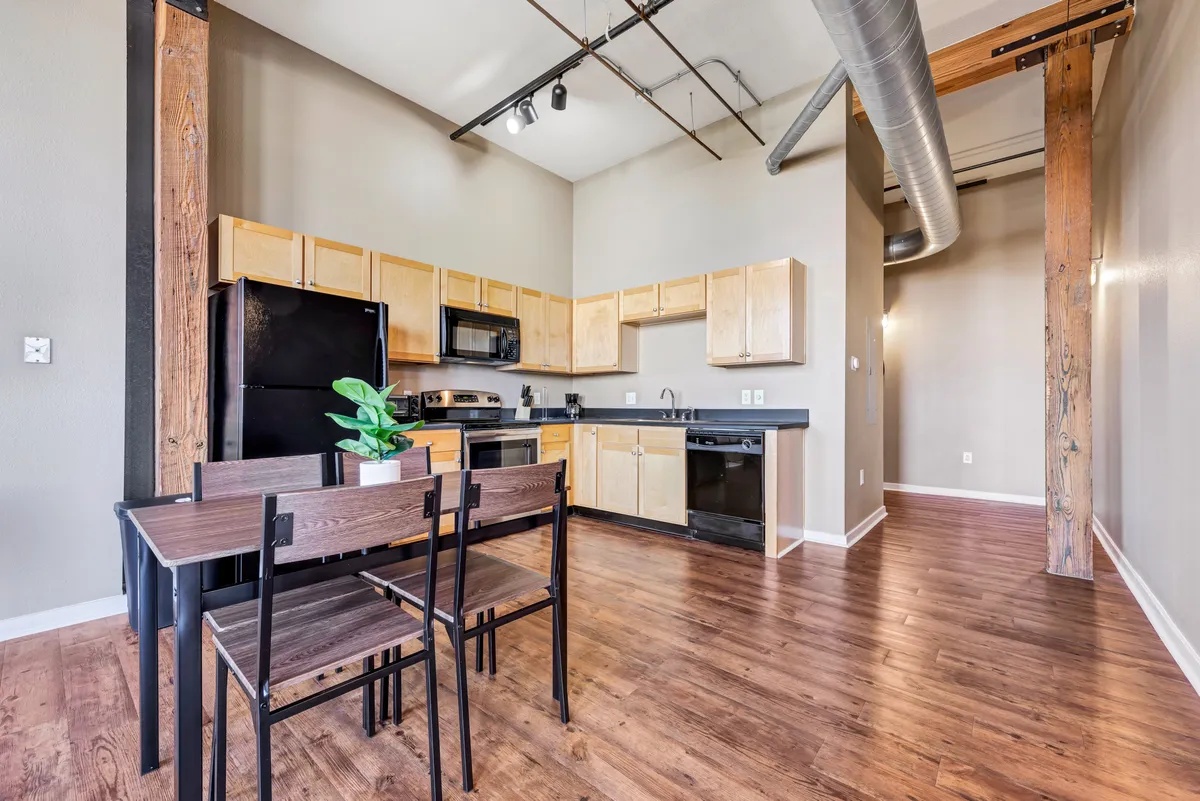 A cozy kitchen and dining area featuring a wooden-beamed ceiling, a central dining table, and a clearly defined kitchen zone. The atmosphere is intimate and designed for sharing meals, with architectural elements that nod to the apartment’s historical character.
