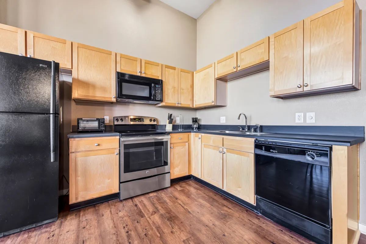 A warmly lit kitchen featuring stainless steel appliances, sleek black countertops, and wooden cabinets. The space balances modern convenience with an inviting atmosphere, suggesting both functionality and a welcoming setting for cooking or entertaining.